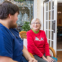 A male nurse sitting and chating with a resident in a Christmas sweater